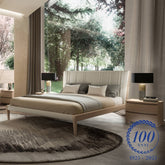 Letto matrimoniale in legno chiaro con testiera imbottita in pelle bianca, collezione Modigliani, ambientato in una camera luminosa con vista sul giardino. Edizione centenario 1925–2025.